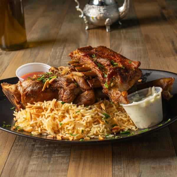Olivo Mediterranean Cuisine's lamb shank with rice, almonds, and two dipping sauces on a black plate.