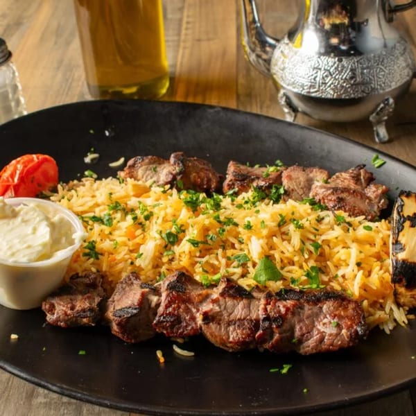 Olivo Mediterranean Cuisine's grilled lamb skewers with seasoned rice, a side of sauce, and grilled tomato.