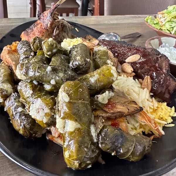 A large platter of Middle Eastern food, including stuffed grape leaves, rice, lamb, and ribs.